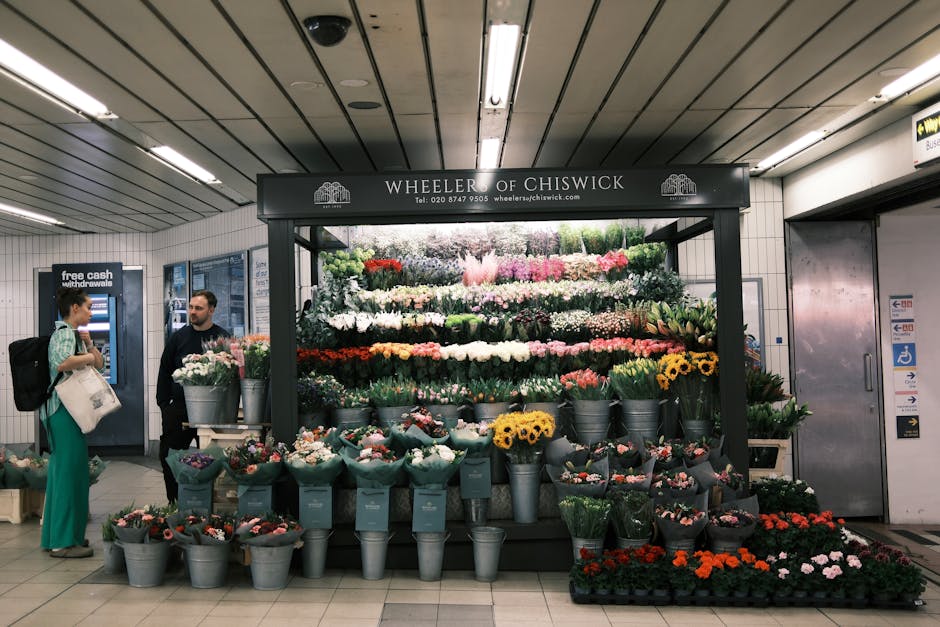 A vibrant flower stall located in a train station, featuring a variety of fresh floral arrangements and bouquets. The display includes multicolored flowers such as white, pink, red, purple, yellow, an