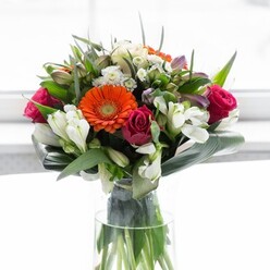 This masterfully rendered bouquet, a true reflection of Temple's refined sensibilities, overflows with a rich palette that instantly uplifts the senses. Gentle peach and creamy gerbera daisies radiate outward, their soft petals mellowing the fiery orange companions-they form a luminous crown around the more dramatic, fuchsia roses whose tightly packed spirals evoke a classic London romance. Threaded throughout the arrangement, tufts of white alstroemeria and pale pink blossoms lend a delicate grace, their lightness providing a refreshing contrast to the saturated tones. Broad, dark green aspidistra leaves curve protectively around the base, recalling the sheltering canopies of trees throughout Temple's tranquil gardens, while gently pointed foliage interspersed throughout creates a harmonious, natural rhythm. The clear glass vase, elongated and elegant, displays sturdy green stems and the occasional glint of water, asserting the bouquet's freshness and craftsmanship. Illuminated by soft, white ambient light-like the glow from a morning window above a bustling Temple café-the design feels both vibrant and soothing. This bouquet, meticulously assembled by Florist Temple, is the embodiment of celebration and appreciation, ideal for enhancing a legal office reception, gifting on Barrister's graduation, or simply bringing joy into a Temple townhouse. Each detail pays homage to the area's blend of tradition and modernity.